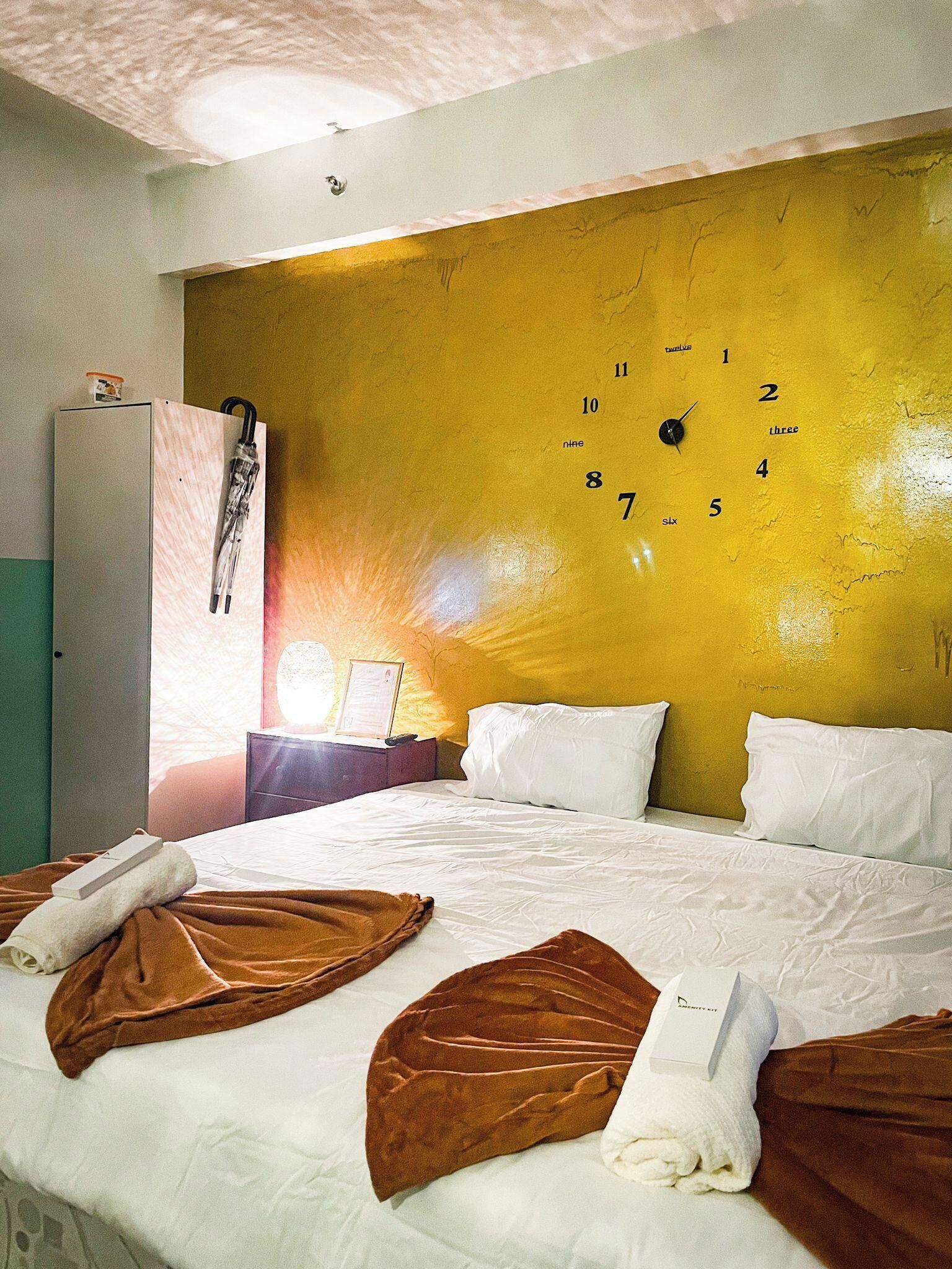 A hotel room with a large bed, a nightstand, a wardrobe, and a wall clock.