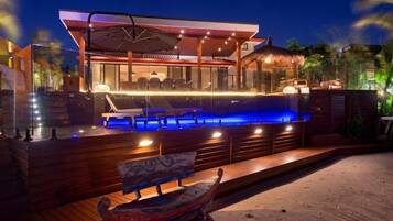 A modern outdoor pool area with a wooden deck, lounge chairs, and a boat.