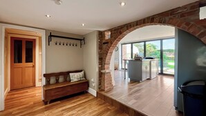 A spacious living area with a wooden floor, a stone archway, a bench, and a kitchen area with a view of the outdoors.