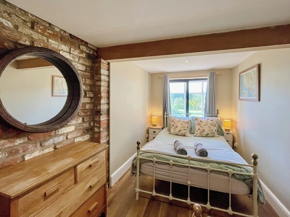 A bedroom with a brick wall, a wooden dresser, a metal bed frame, and a window with curtains.