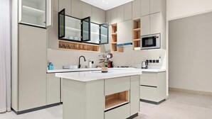 A modern kitchen with a central island, built-in microwave, and open shelving.