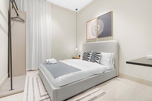 A modern bedroom with a bed, a bedside table, a hanging light, and a framed artwork on the wall. - Silkhaus Al Mahmal 70 (Riyadh)