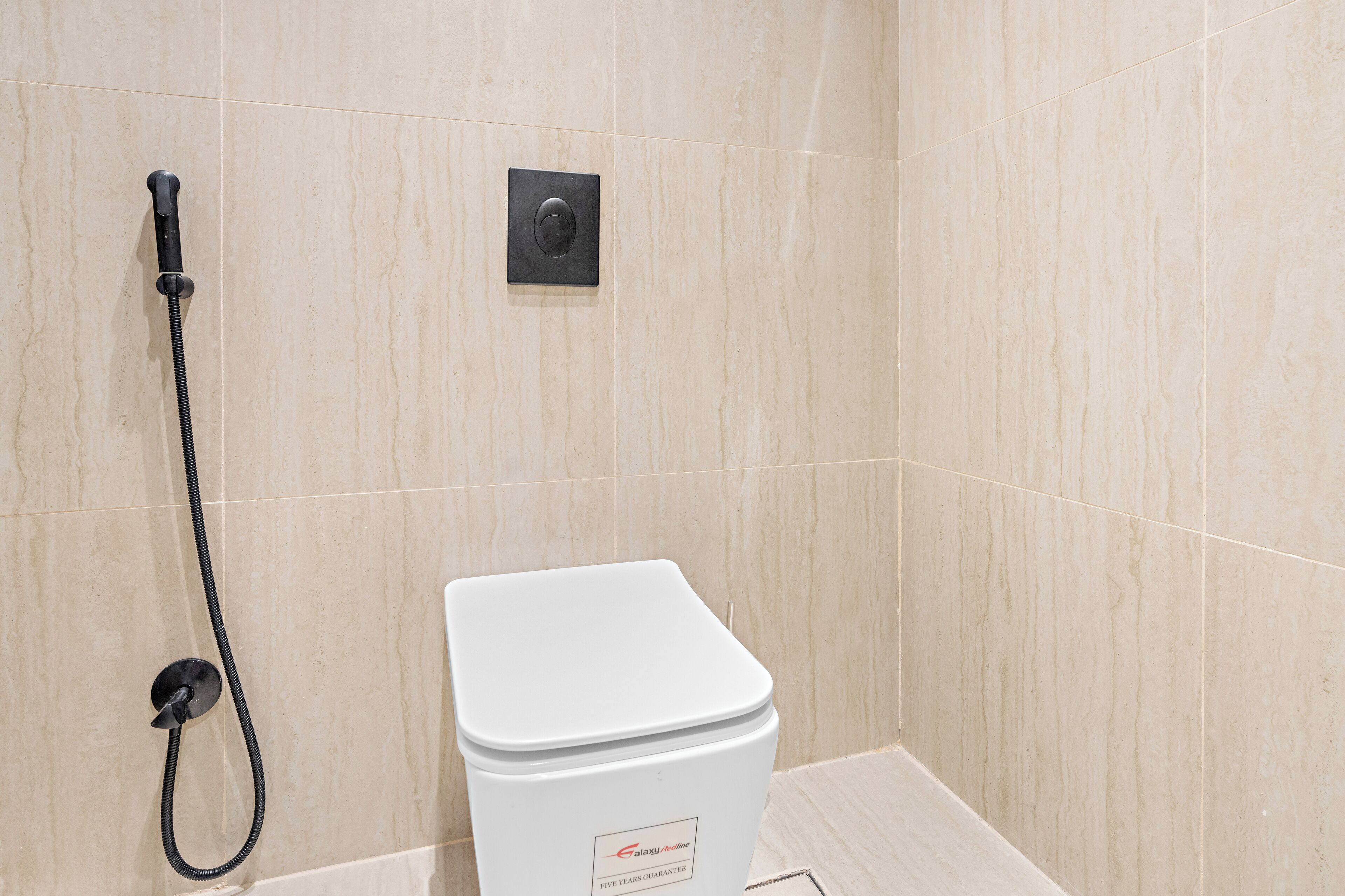 A bathroom with a white toilet, a handheld showerhead, and a control panel on the wall.