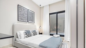 A modern bedroom with a large bed, a nightstand, a wall-mounted light, and two framed artworks.