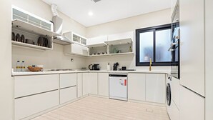 Uma cozinha moderna com armários brancos, lava-louças, máquina de lavar roupa e uma janela com vista.