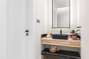 A modern bathroom with a black sink, wooden countertop, and a large mirror. There is a basket under the countertop and a small plant on the sink. - Silkhaus Ramz 49 (Riyadh)