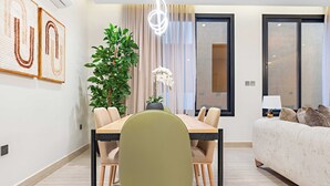 Uma área de jantar moderna com uma mesa e cadeiras, uma planta em vaso e um sofá ao fundo.