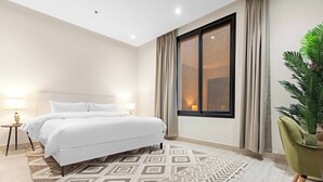 Quarto de hotel moderno com uma cama grande, janela com cortinas, uma cadeira verde e um tapete estampado.