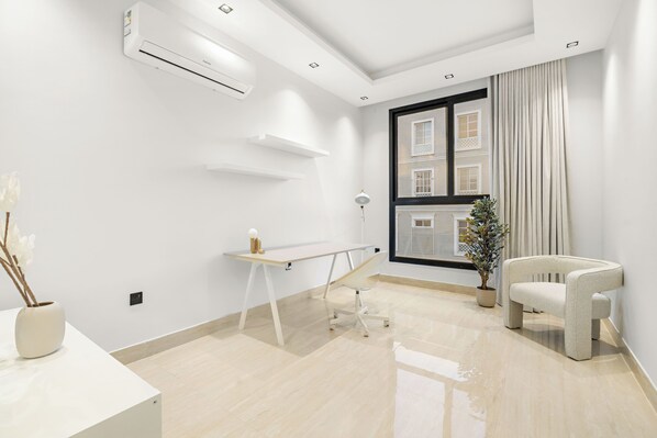 A modern, minimalist room with a white desk, a white chair, a potted plant, and a large window with curtains. - Silkhaus Safa 47 D (Riyadh)