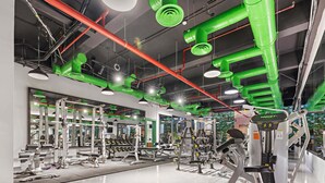 A gym with various exercise equipment, green and red pipes on the ceiling, and large mirrors on the walls. - Silkhaus Safa 47 A (Riyadh)