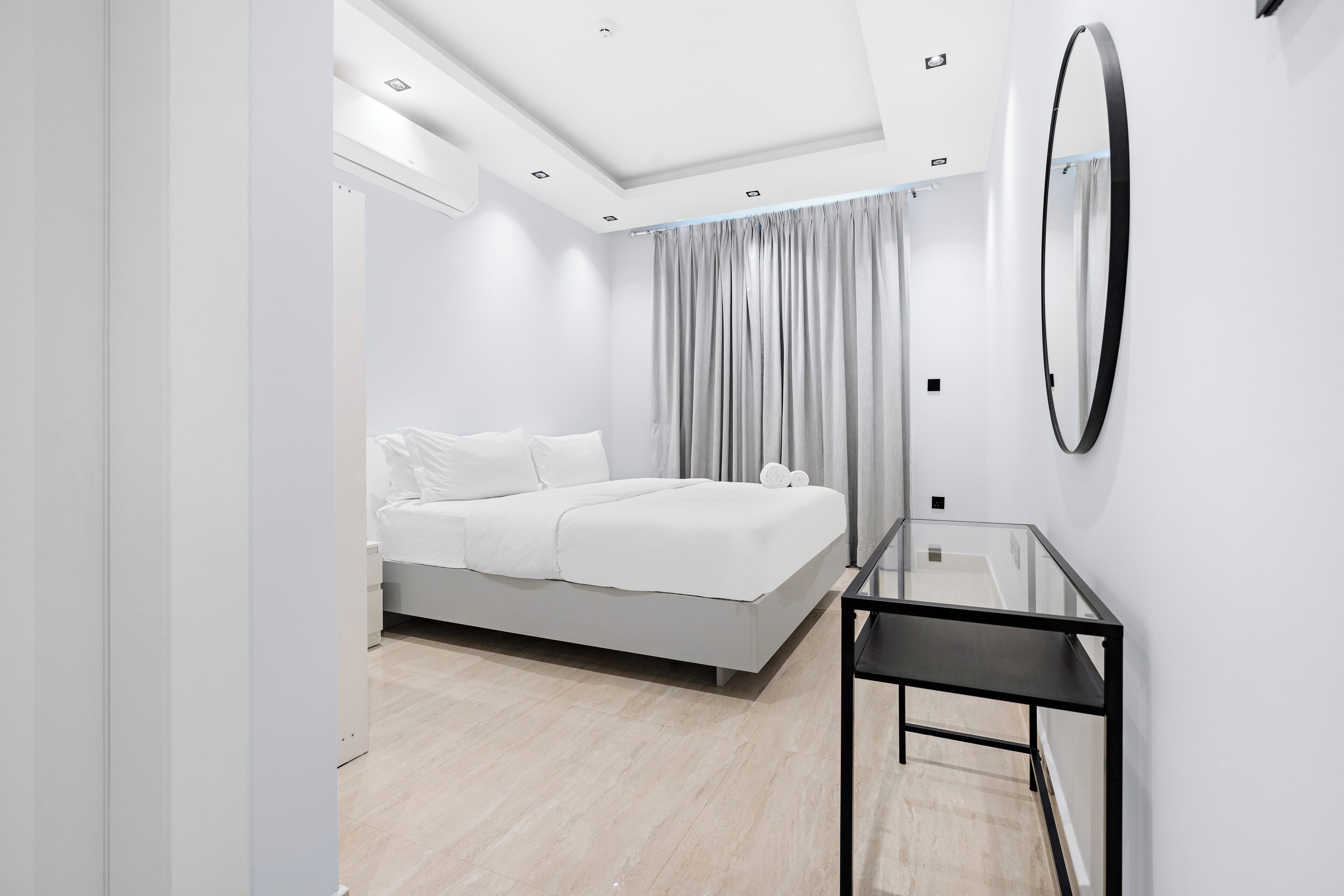 A modern bedroom with a bed, a glass table, and a large mirror on the wall.