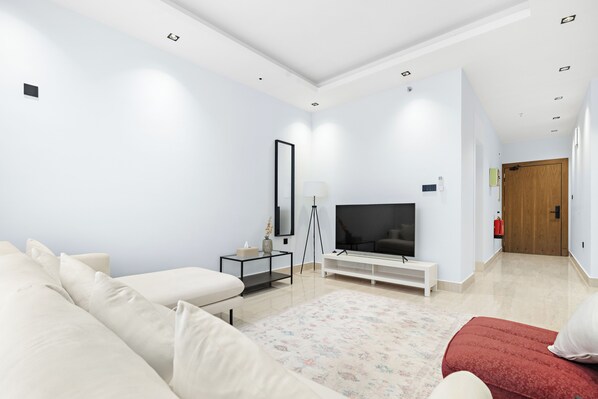 Un salon moderne avec un canapé, un pouf rouge, un téléviseur, une lampe sur pied et une console blanche.