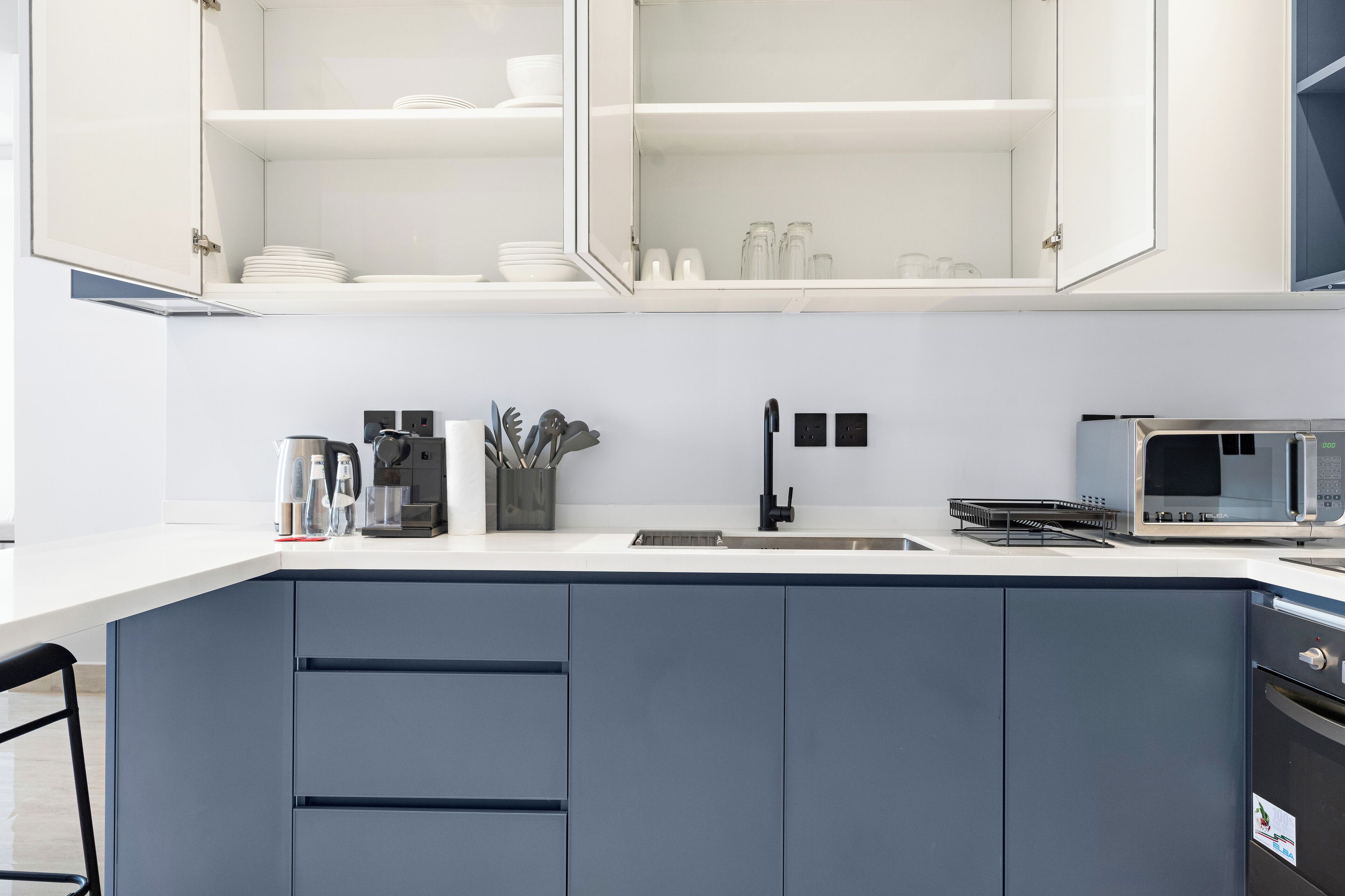 A modern kitchen with grey cabinets, a white countertop, a built-in microwave, and a coffee maker.