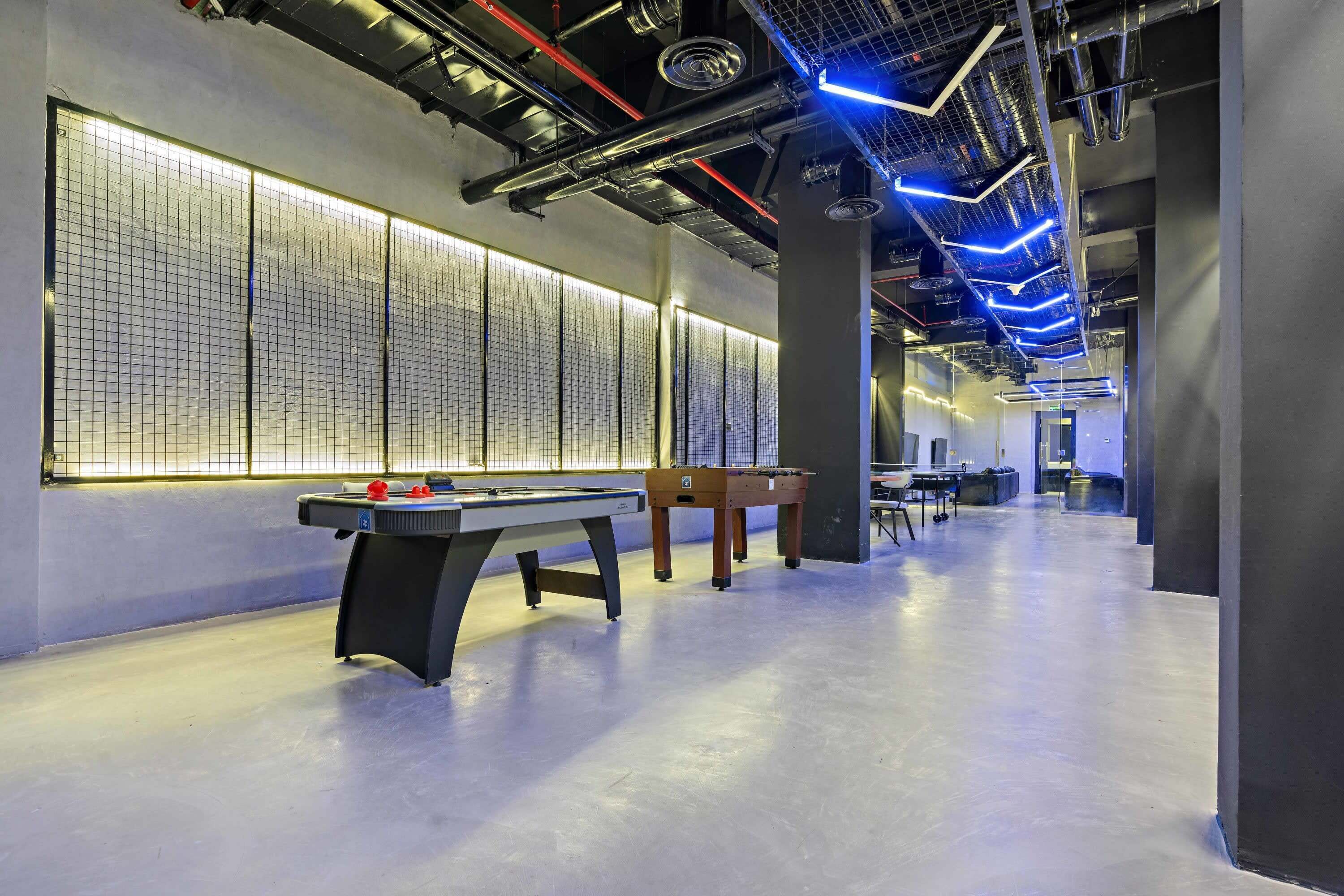 Un espace intérieur moderne doté d’une table de billard, d’un baby-foot et d’un long couloir éclairé par des luminaires encastrés au plafond.