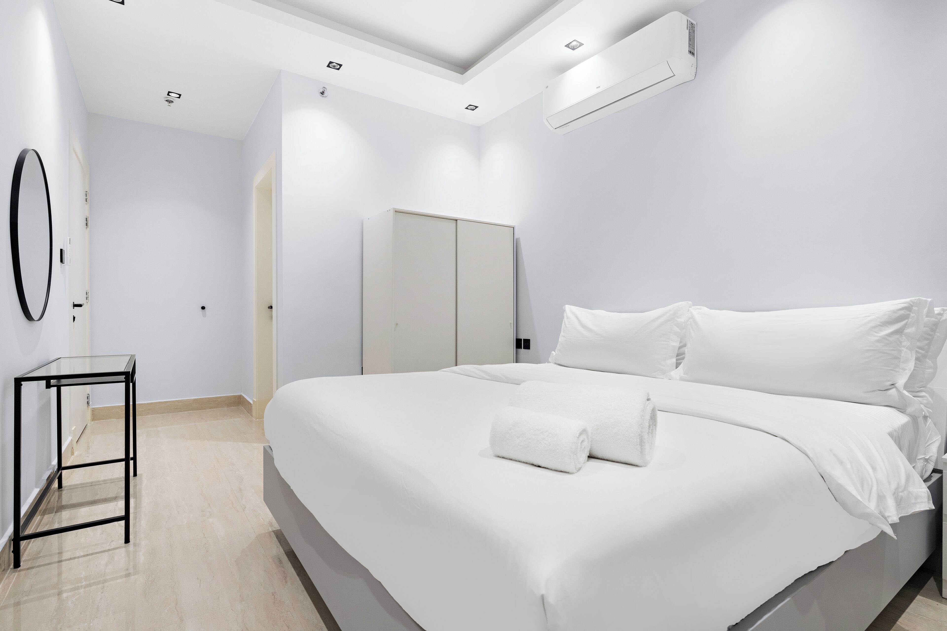 Ein modernes Schlafzimmer mit einem großen Bett, einem kleinen Tisch, einem Kleiderschrank und einer Klimaanlage.