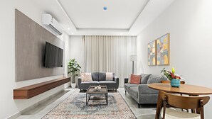 A modern living room with a flat-screen TV, grey sofas, a coffee table, and a dining table with chairs. - Silkhaus Sayl 25 (Riyadh)