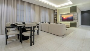 A modern living room with a dining area, a large flat-screen TV mounted on a wall, and a sofa set. - Silkhaus Majidia 127 (Riyadh)