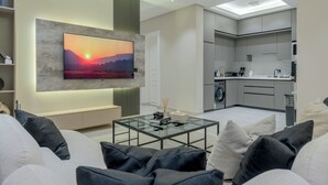 A modern living room with a large flat-screen TV mounted on a textured wall, a glass coffee table, and a sofa with cushions. - Silkhaus Majidia 127 (Riyadh)