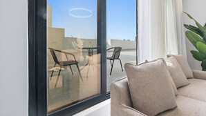 A modern living room with a sofa and a large window overlooking a balcony with outdoor furniture. - Silkhaus Majidia 139 (Riyadh)