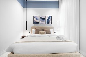 A modern bedroom with a large bed, white bedding, a headboard, and three abstract paintings on the wall. - Silkhaus Majidia 139 (Riyadh)