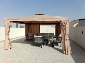 A rooftop terrace with a beige canopy, a sofa, two armchairs, and a small table. - Silkhaus Majidia 139 (Riyadh)