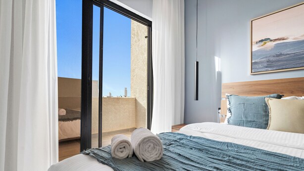 A hotel room with a bed, a view of the city, and a painting on the wall. - Silkhaus Majidia 139 (Riyadh)