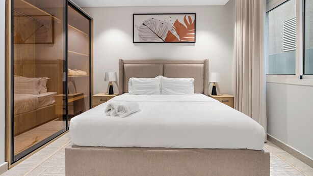 A modern bedroom with a large bed, a glass door closet, and a framed artwork on the wall. - Silkhaus Majidia156 (Riyadh)