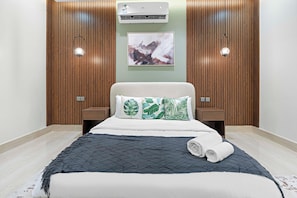 Un dormitorio moderno con una cama, aire acondicionado instalado en la pared y un cuadro abstracto enmarcado.