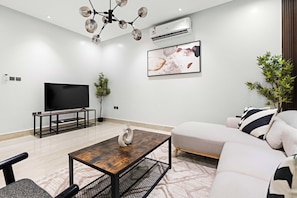 Una sala de estar moderna con un televisor de pantalla plana, una mesa de centro de madera, un sofá y una planta grande.