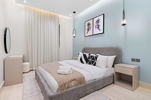 Ein modernes Schlafzimmer mit einem großen Bett, Nachttischen, einem an der Wand montierten Fernseher und einer Deckenleuchte.