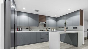 A modern kitchen with grey cabinets, a white countertop, and a built-in oven. - Silkhaus Rose Residency 36 (Riyadh)