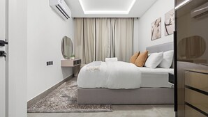 A modern bedroom with a bed, bedside table, and a mirror. - Silkhaus Rose Residency 36 (Riyadh)