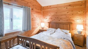 Quarto de cabana de madeira com cama, mesas de cabeceira e janela com cortinas.