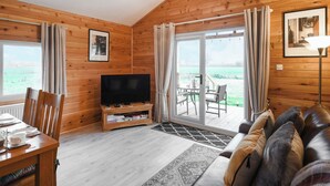 Um quarto acolhedor em estilo cabana, com paredes de madeira, televisão, mesa de jantar com cadeiras, sofá e uma grande porta de vidro deslizante que dá para uma área externa.