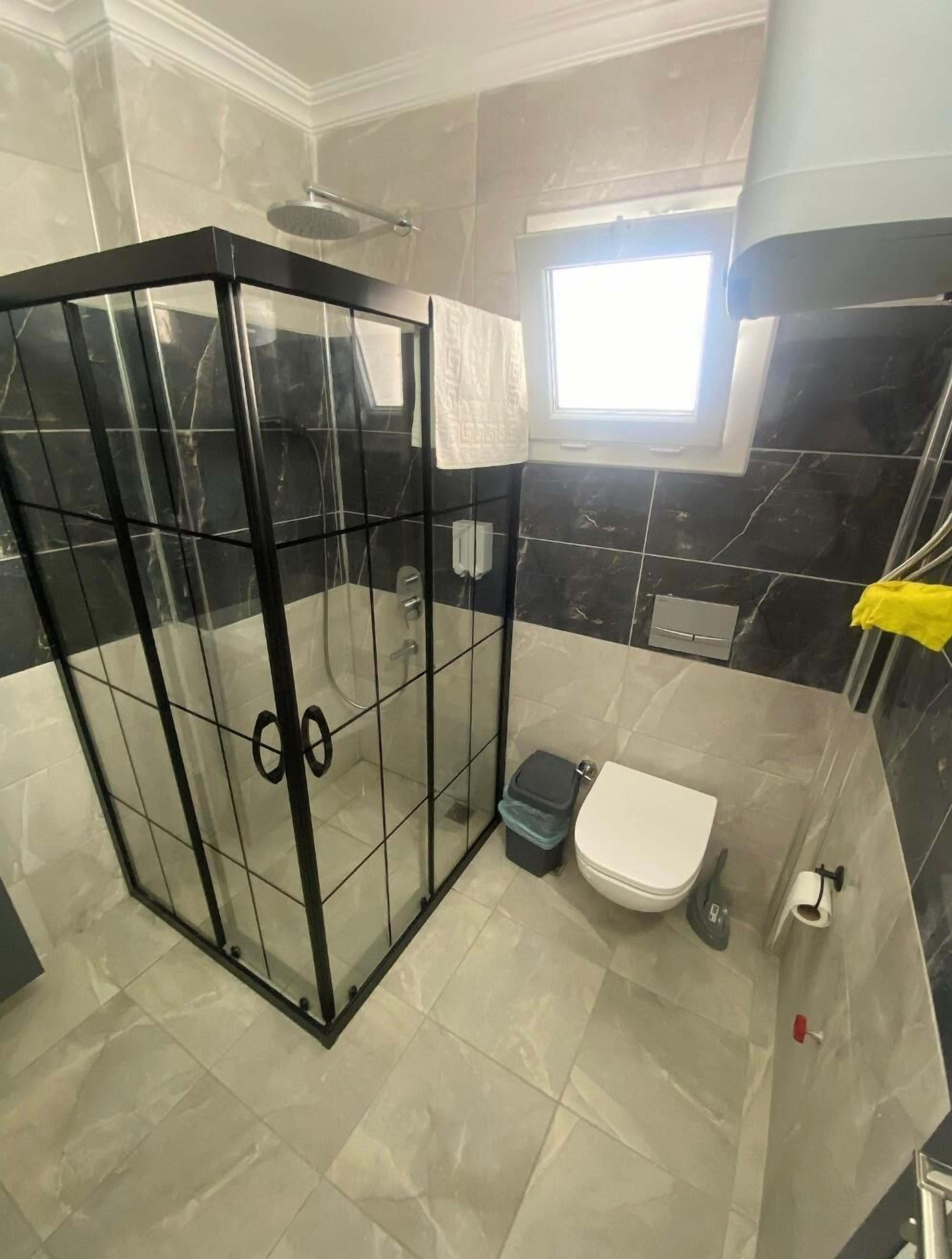 A bathroom with a glass-enclosed shower, a toilet, and a window.