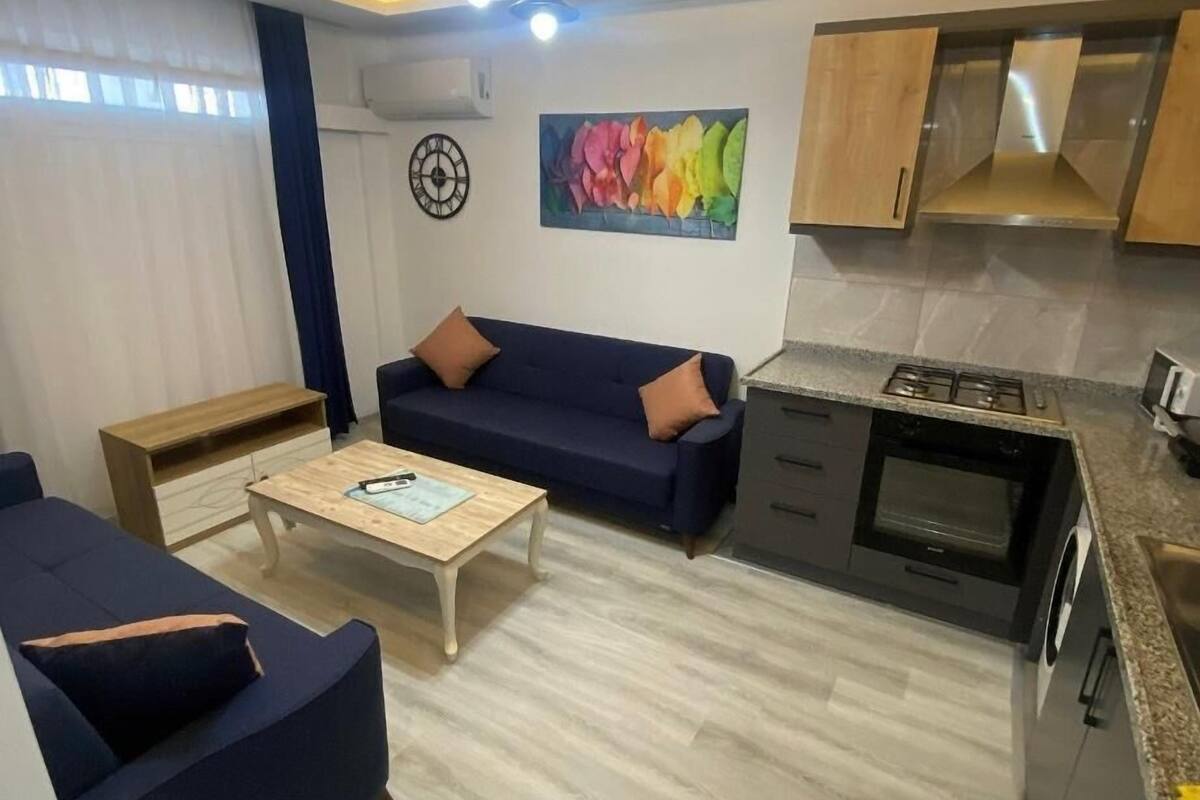 A modern living room with a sofa, a coffee table, and a kitchen area with a stove and cabinets.