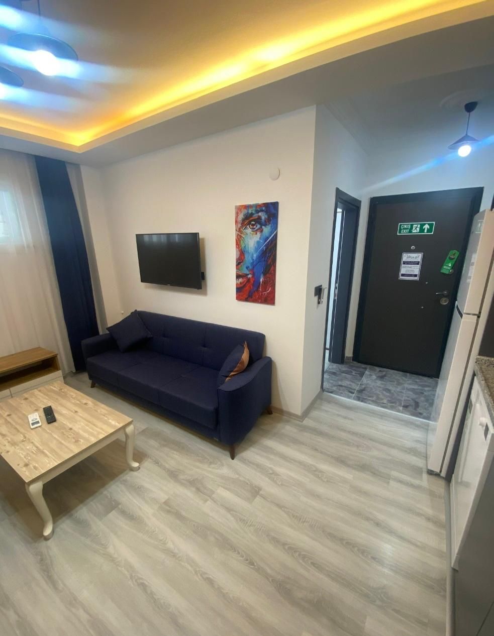 Una sala de estar moderna con un sofá azul oscuro, una mesa de centro de madera y un televisor de pantalla plana montado en la pared.