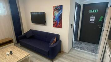 Una sala de estar moderna con un sofá azul oscuro, una mesa de centro de madera y un televisor de pantalla plana montado en la pared.