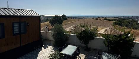 Um terraço no telhado com chão de azulejos, uma mesa e cadeiras, e vista para a paisagem ao redor.