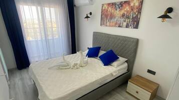 Un dormitorio con cama, mesita de noche, lámpara de pared, un cuadro y ventana con cortinas.