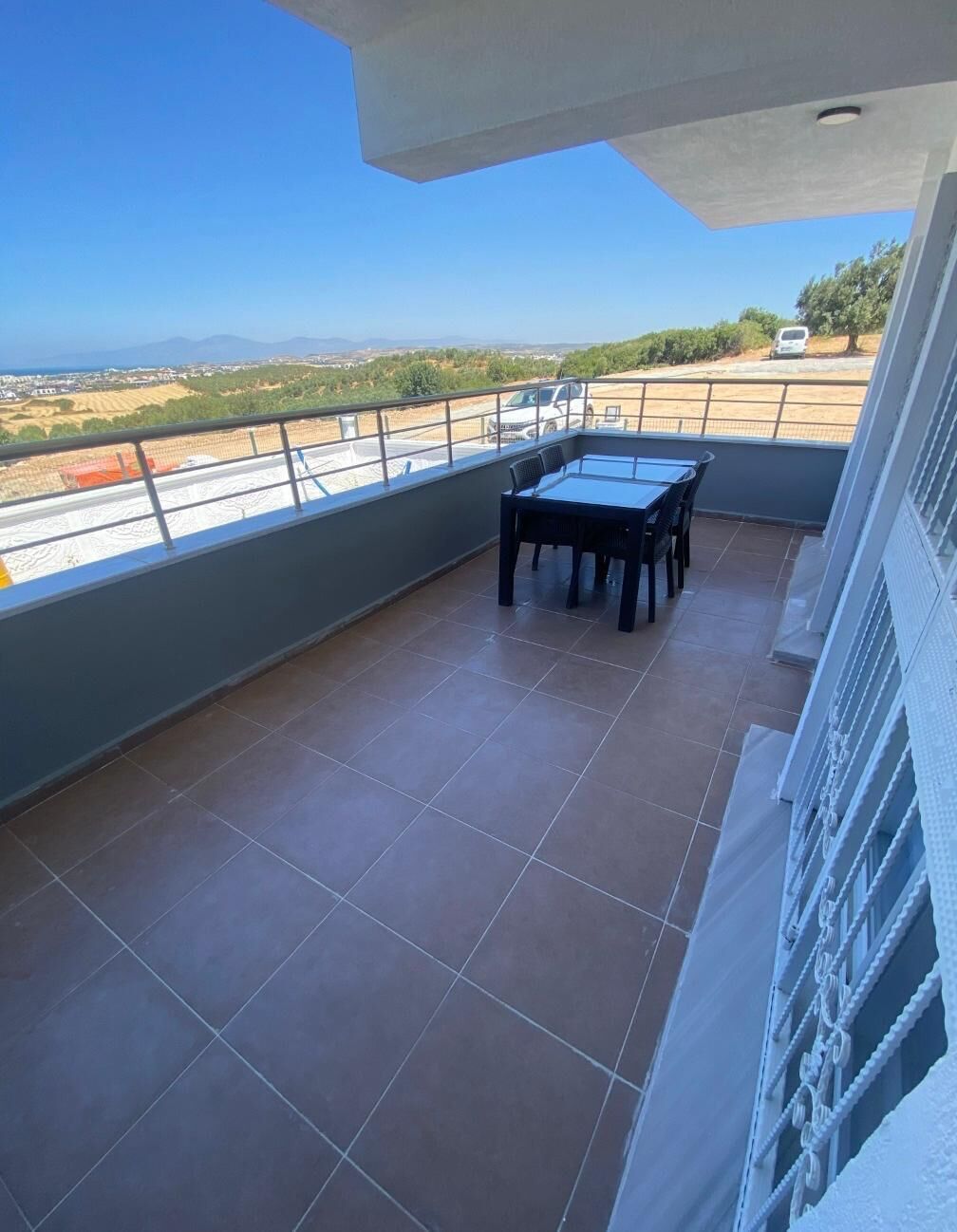 Uma varanda com mesa e cadeiras, vista para o campo e guarda-corpo.