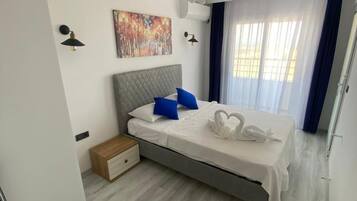 Una habitación de hotel moderna con una cama, una mesita de noche, un ventilador de techo, una lámpara de pared, un cuadro y una ventana con cortinas.