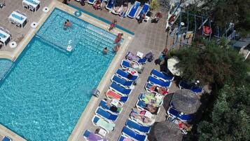 Relax by the pool surrounded by lounge chairs and umbrellas, with a children's play area nearby.