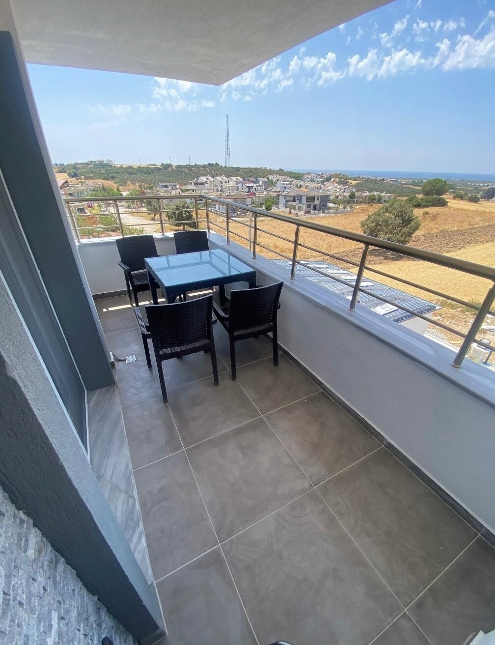 A balcony with a table and chairs, offering a view of a town and the sea.