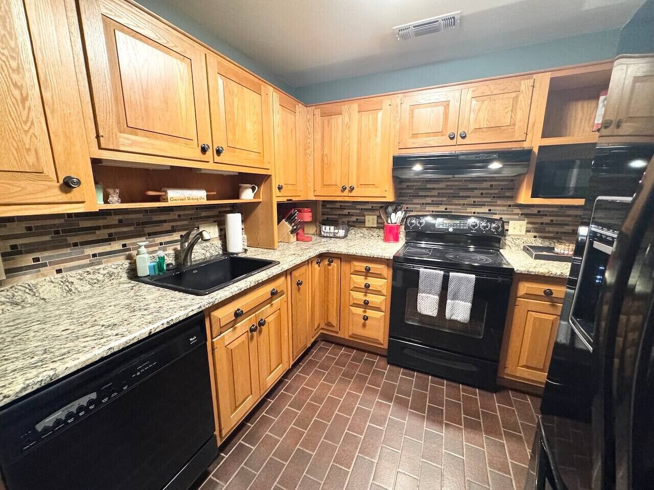 A kitchen with wooden cabinets, a granite countertop, a black stove, and a dishwasher.