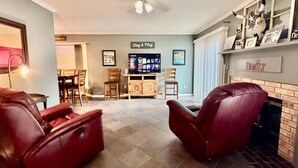 Un salon avec deux fauteuils inclinables en cuir, une cheminée et un téléviseur en arrière-plan.
