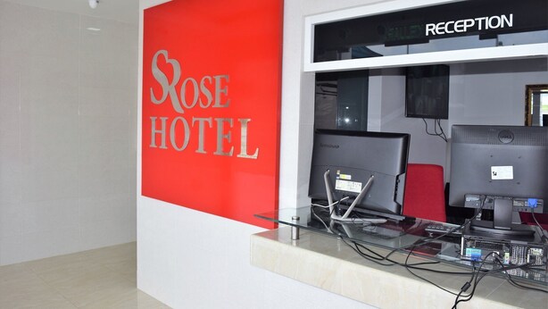 Mostrador de recepción con un letrero rojo para Rose Hotel, dos monitores Lenovo y una computadora Dell.