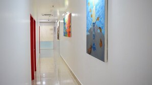 Un pasillo con paredes blancas, una puerta roja y dos cuadros.
