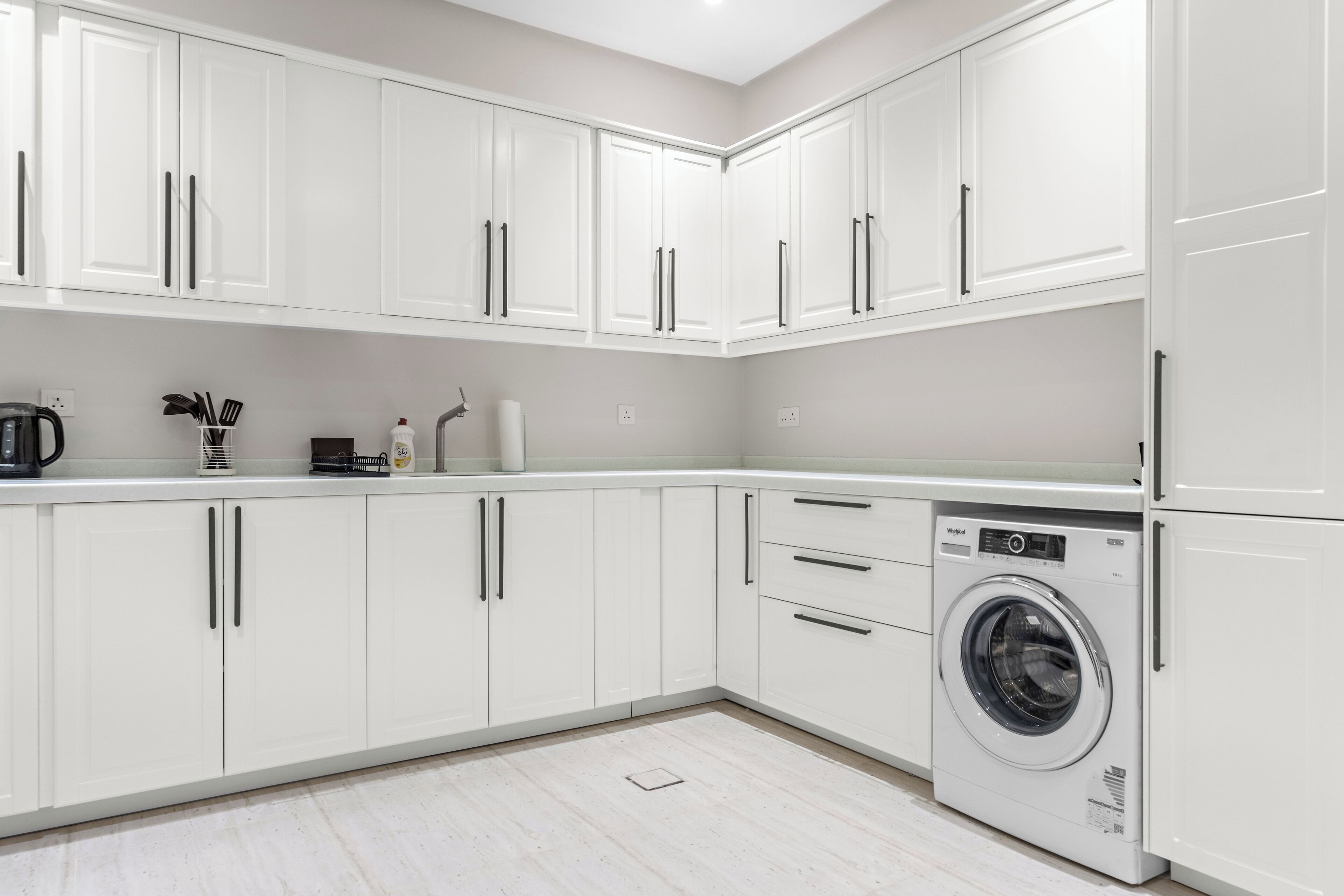 A modern kitchen with white cabinets, a built-in washing machine, and a countertop with kitchen appliances.