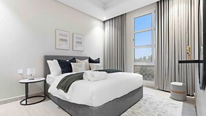 Ein modernes Hotelzimmer mit einem großen Bett, einem runden Beistelltisch, einem kleinen Hocker und einem großen Fenster mit Vorhängen.